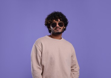 Photo of Handsome young man in sunglasses on violet background