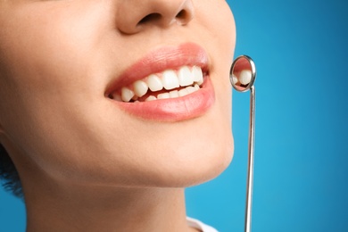 Photo of Young woman with mouth mirror on blue background, closeup. Cosmetic dentistry