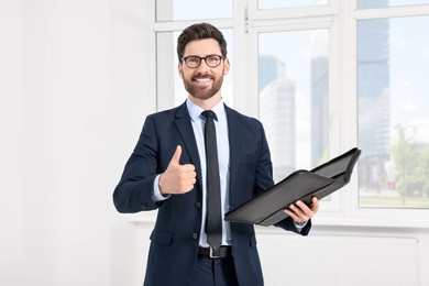 Handsome real estate agent with documents showing thumbs up indoors