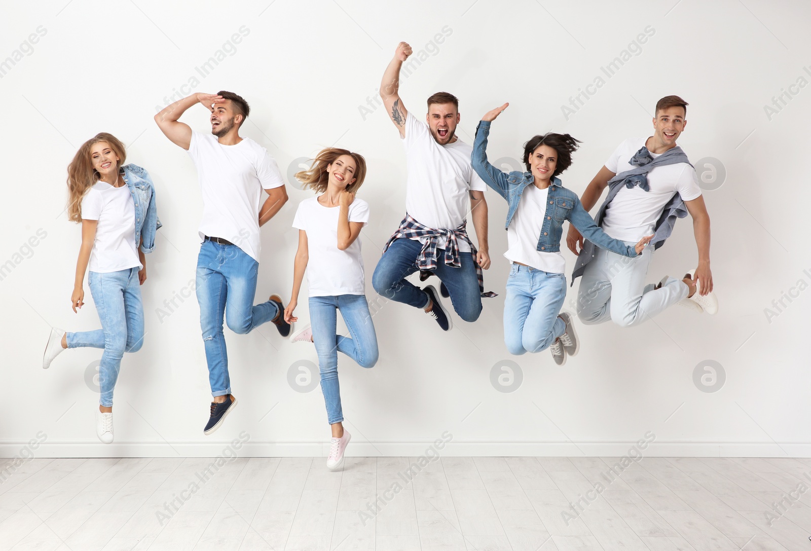 Photo of Group of young people in jeans jumping near light wall