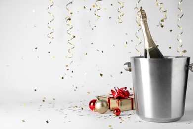Photo of Happy New Year! Bottle of sparkling wine in bucket, gift box and festive decor on white background, space for text