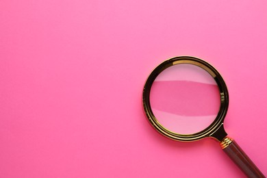 Magnifying glass on pink background, top view. Space for text