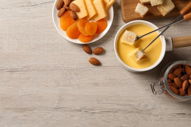 Pot of tasty cheese fondue and snacks on light wooden table, flat lay. space for text