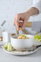 Woman decorating delicious celery soup at white table, closeup