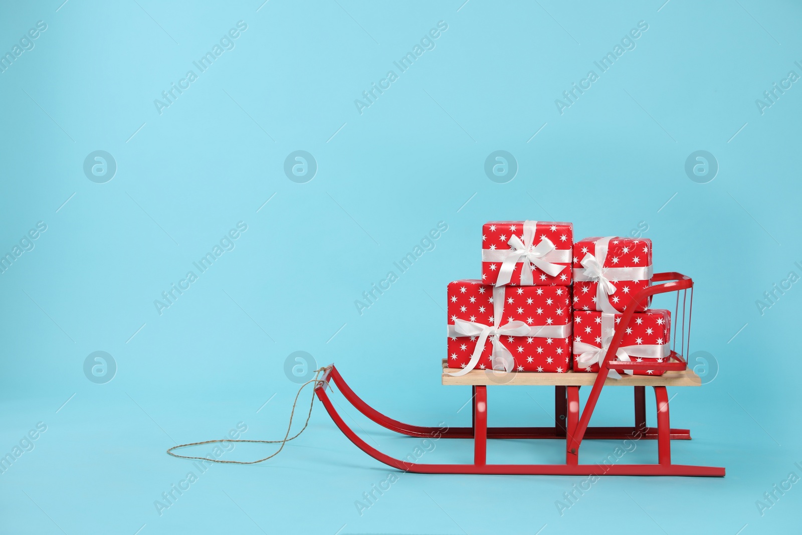 Photo of Stylish sleigh with Christmas gifts on light blue background, space for text