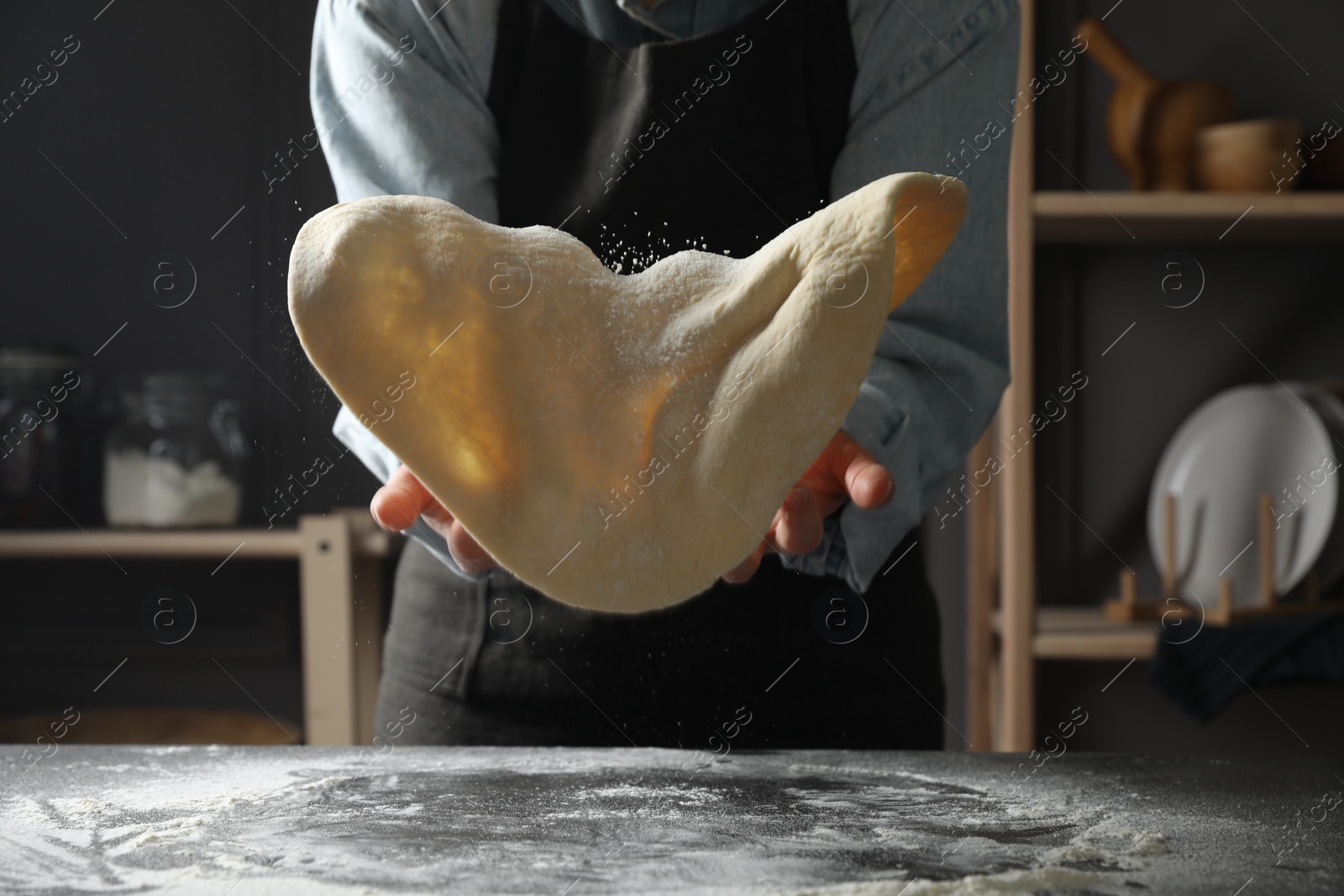 Photo of Woman tossing pizza dough at table in kitchen, closeup