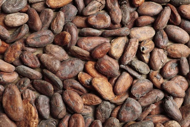 Tasty cocoa beans as background, top view