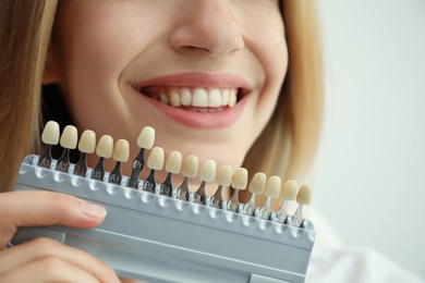 Photo of Woman matching teeth color with palette on white background, closeup. Cosmetic dentistry