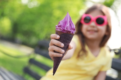 Cute little girl with delicious ice cream on bench in park, space for text