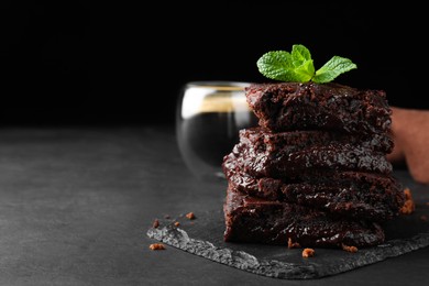 Photo of Delicious chocolate brownies with fresh mint on black table. Space for text