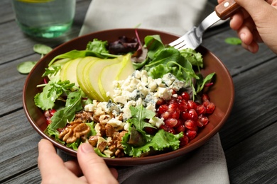 Photo of Woman with tasty pear salad at black wooden table, closeup