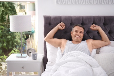 Photo of Happy man waking up after sleeping on comfortable pillow in bed at home