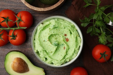 Photo of Bowl of delicious guacamole and ingredients on wooden table, flat lay