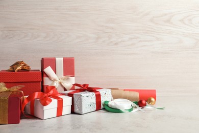 Beautiful Christmas gift boxes wrapped in paper and decorated with bows on light table, space for text