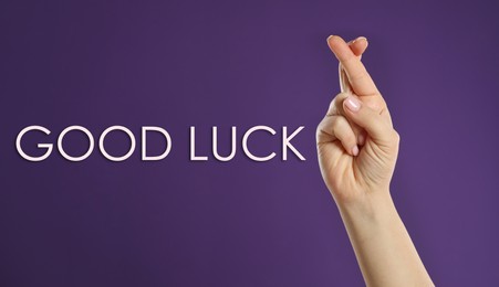 Image of Woman with crossed fingers on violet background, closeup. Good luck superstition