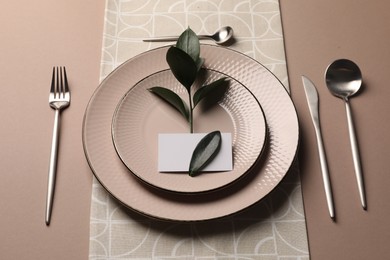 Stylish table setting. Plates, cutlery, blank card and green twig on beige background