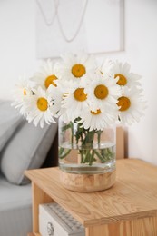 Photo of Bouquet of beautiful daisy flowers on wooden nightstand in bedroom