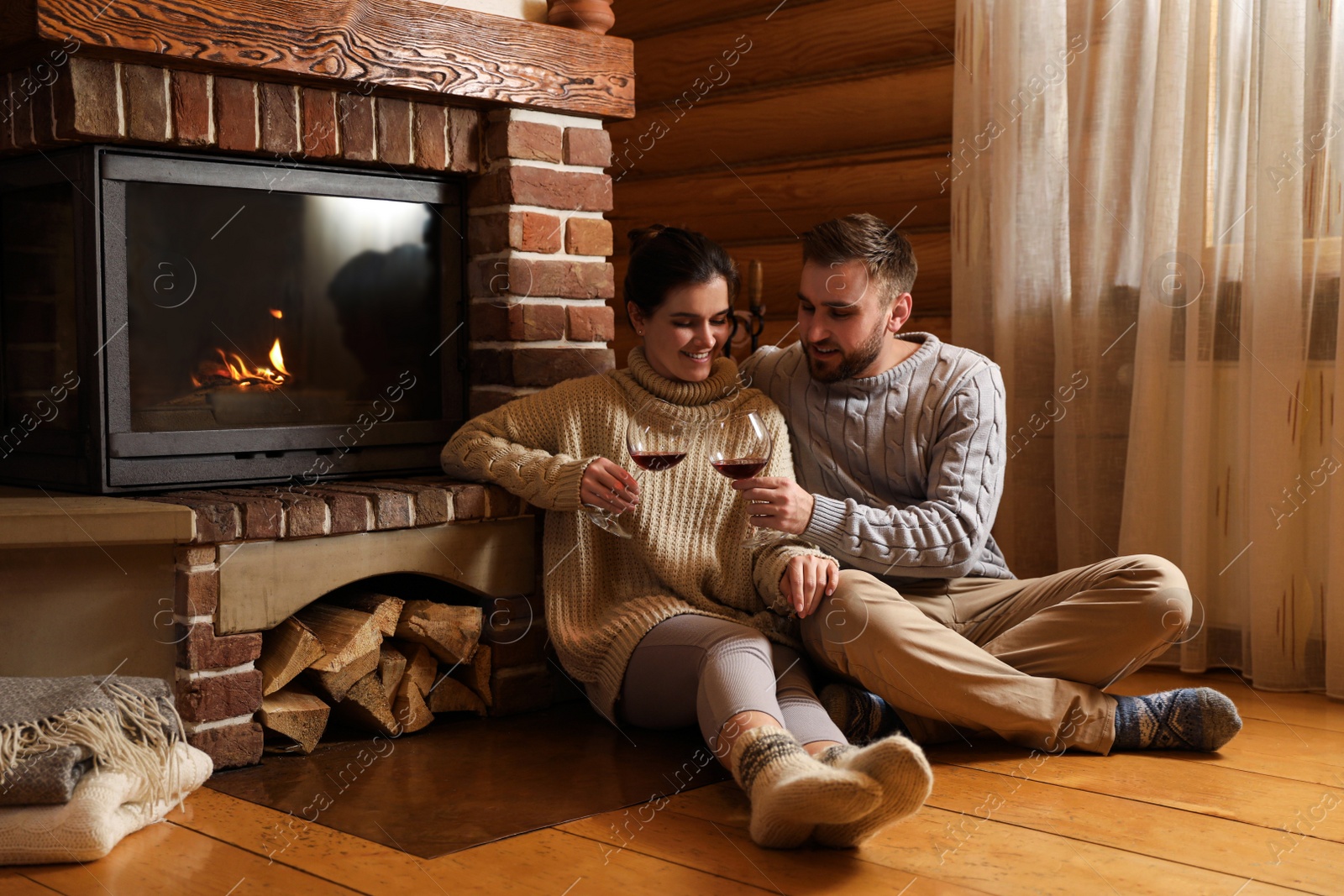 Photo of Lovely couple with glasses of wine near fireplace at home. Winter vacation