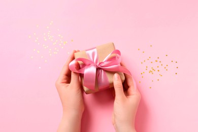 Photo of Woman with gift box and confetti on pink background, top view