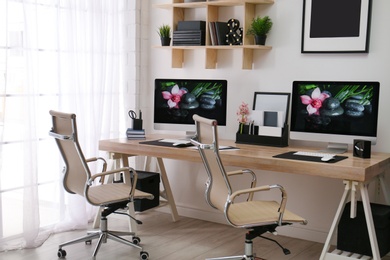 Photo of Modern workplace with large desk and computers in room. Stylish interior