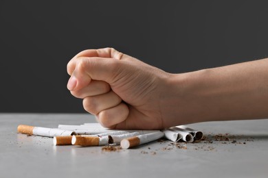 Photo of Stop smoking concept. Woman crushing cigarettes at gray table, closeup