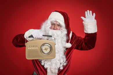 Photo of Santa Claus with vintage radio on red background. Christmas music