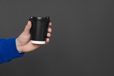 Photo of Man holding takeaway cup with drink on dark grey background, closeup view and space for text. Coffee to go