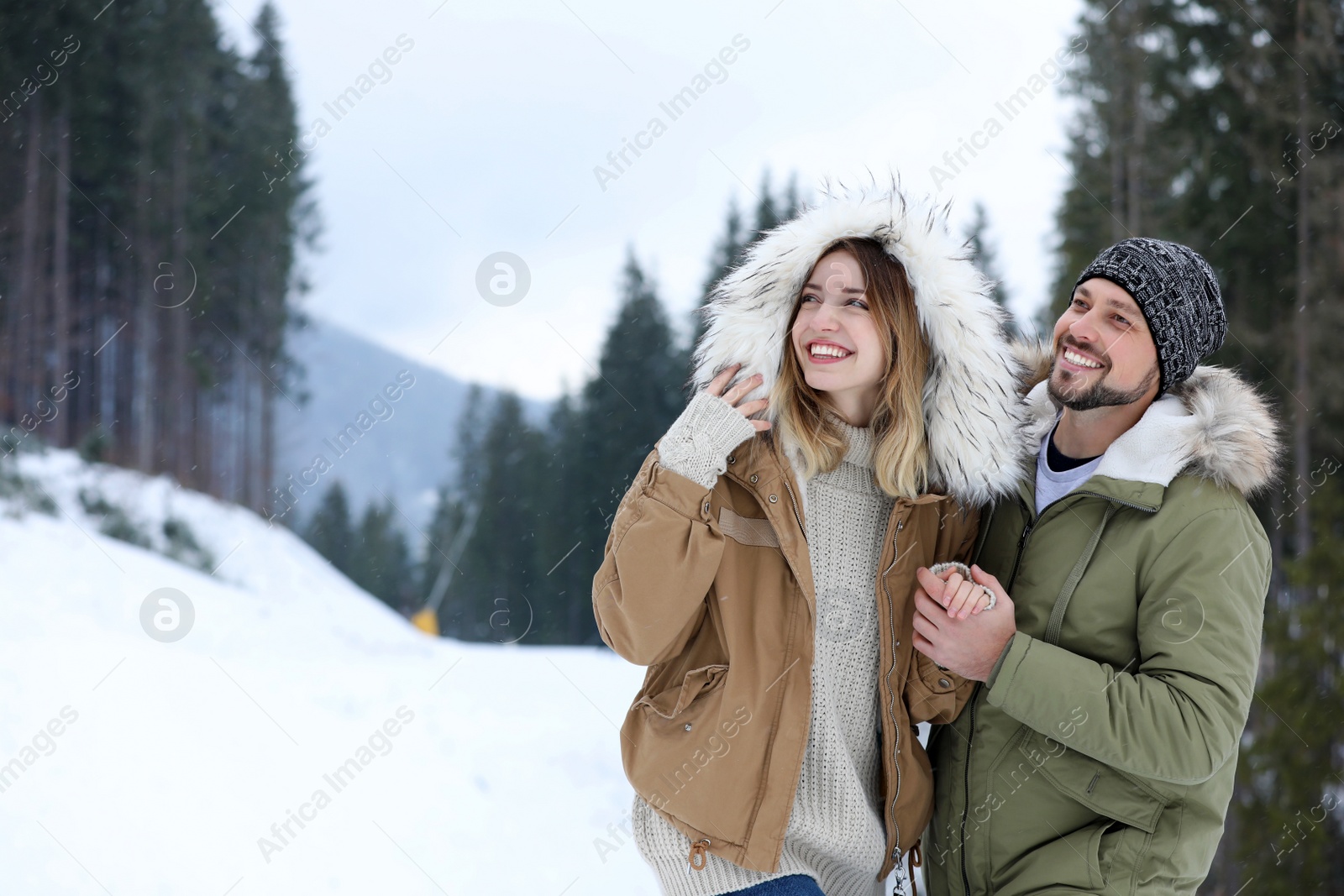 Photo of Happy couple near conifer forest on snowy day, space for text. Winter vacation