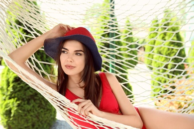 Photo of Young woman relaxing in hammock outdoors on warm summer day