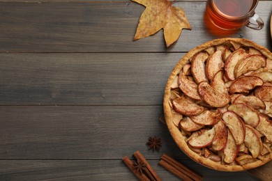 Photo of Delicious apple pie, cup of tea and cinnamon on wooden table, flat lay. Space for text