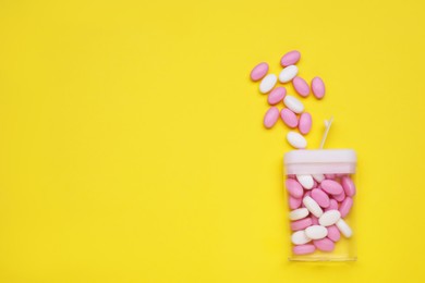 Photo of Tasty dragee candies and container on yellow background, flat lay. Space for text