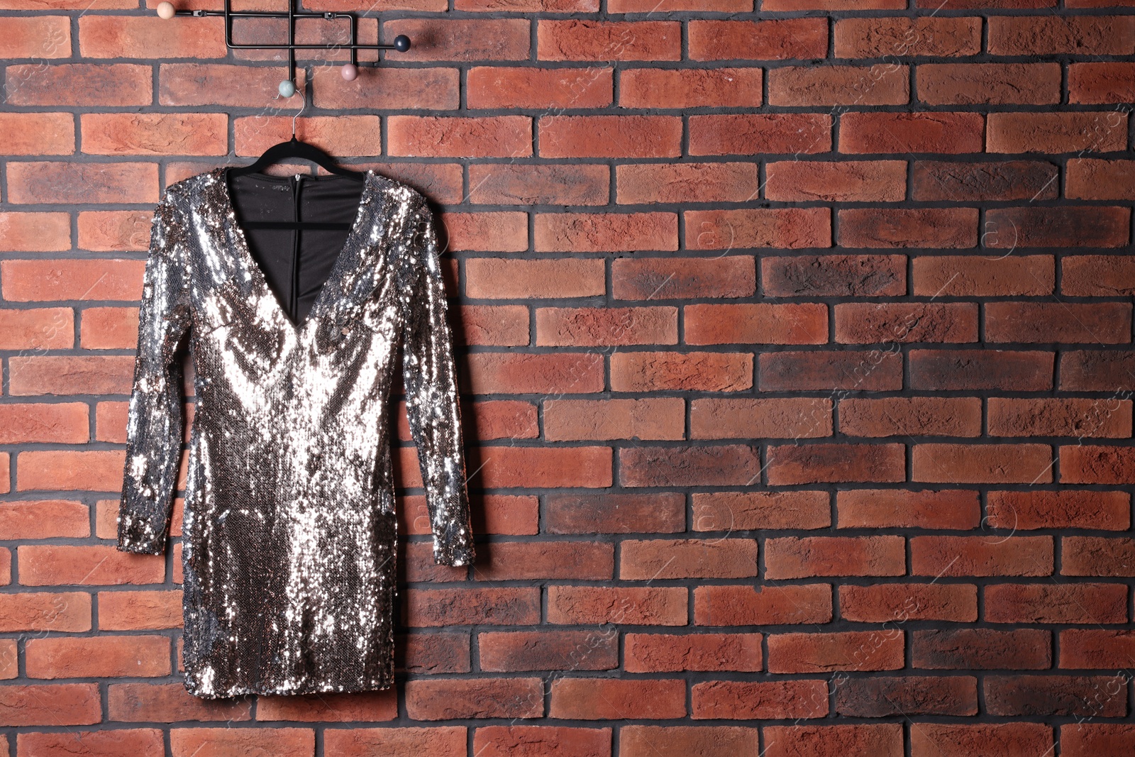 Photo of Beautiful silver women's party dress on hanger near brick wall, space for text. Stylish trendy clothes for high school prom