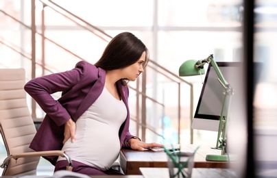 Photo of Young pregnant woman suffering from pain while working in office