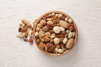 Photo of Bowl with organic mixed nuts on white wooden background, top view