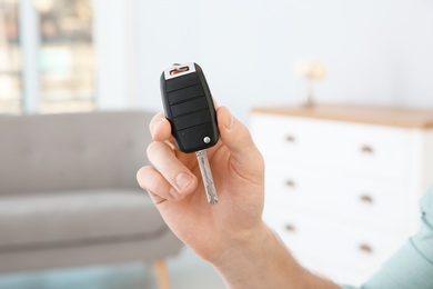Photo of Young man with new car key in dealership, closeup