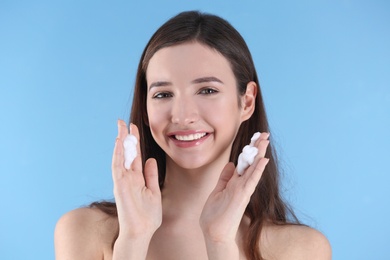 Photo of Teenage girl with acne problem using cream against color background