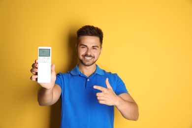 Photo of Happy young man with air conditioner remote control on yellow background