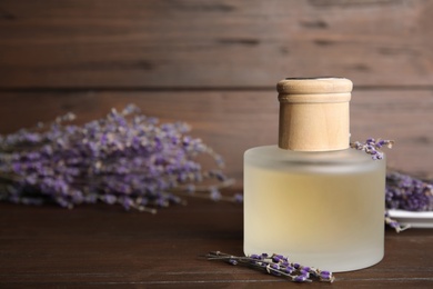 Photo of Bottle with aromatic lavender oil on wooden table. Space for text