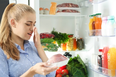 Photo of Woman taking stale meat out of refrigerator in kitchen