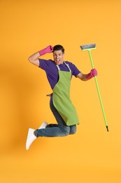 Photo of Man with green broom jumping on orange background