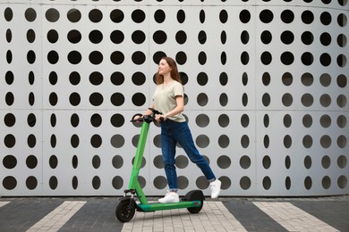 Photo of Happy woman riding modern electric kick scooter on city street