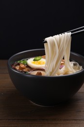 Photo of Eating delicious vegetarian ramen with chopsticks at wooden table against black background