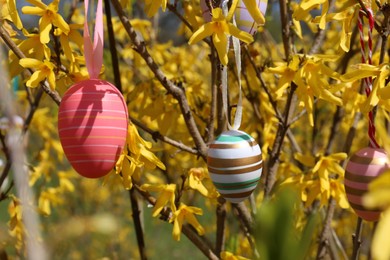 Photo of Beautifully painted Easter eggs hanging on tree outdoors, closeup