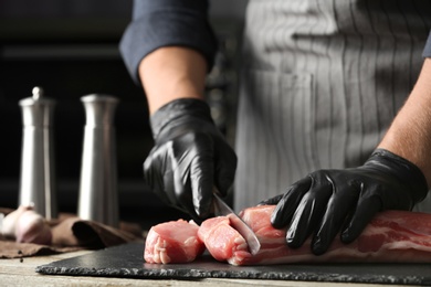 Photo of Man cutting fresh raw meat on wooden table, closeup