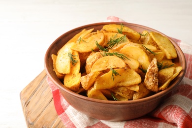 Photo of Bowl of delicious oven baked potatoes with dill on table, closeup