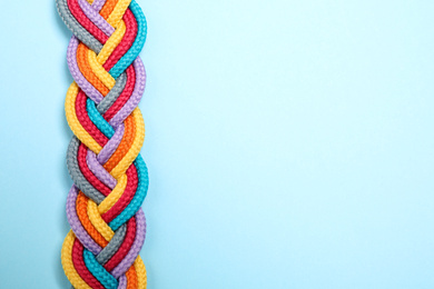 Photo of Top view of braided colorful ropes on light blue background, space for text. Unity concept