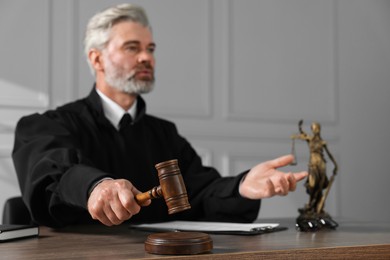 Photo of Judge with gavel and papers sitting at wooden table indoors, selective focus