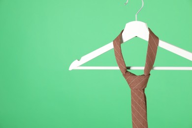 Photo of Hanger with brown striped tie on green background, closeup. Space for text