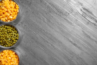 Photo of Open tin cans of conserved vegetables on grey table, flat lay with space for text