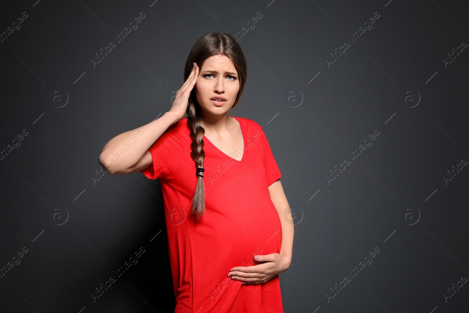 Photo of Young pregnant woman suffering from headache on grey background